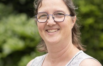 Portret van een vrouw met bril, glimlachend, met een groene, onscherpe achtergrond. (vergroot foto)