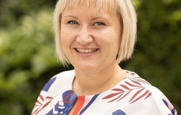 Portret van een lachende vrouw met blond haar, buiten gefotografeerd met groene achtergrond. (vergroot foto)